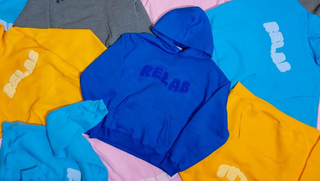 A collection of vibrant hoodies with bold text designs, laid out on a flat surface.