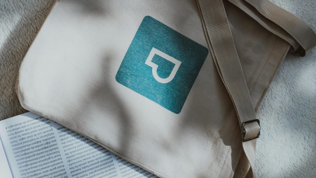 A beige canvas bag displaying a blue logo alongside a printed page. Perfect for branding concepts.